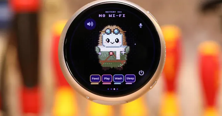 A silver pendant touchscreen computer with a cute little tamagotchi like mascot on screen